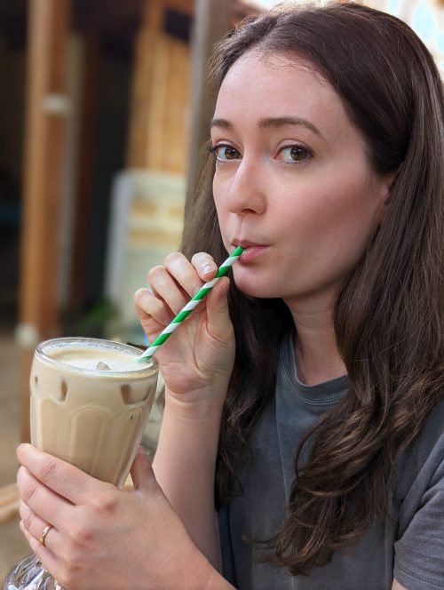 Women drinking an iced chai latte out of a glass, with a green and white straw. 