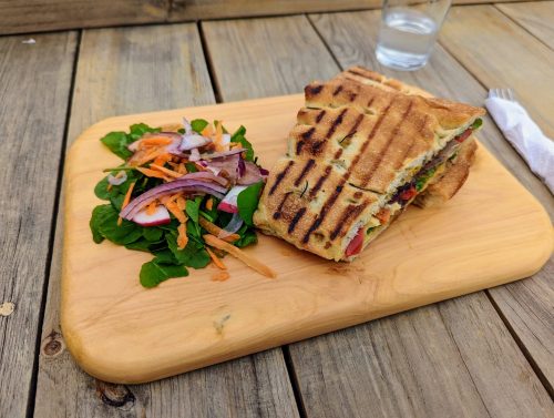 Panini on a wooden board with a green salad on the side. 