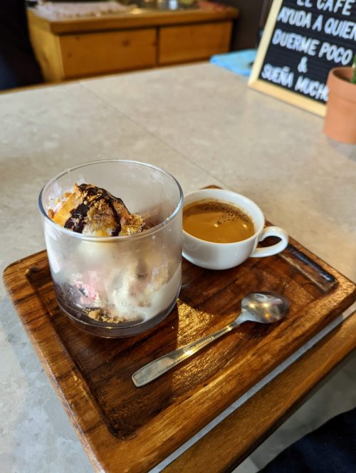 A small glass jar containing ice cream covered in chocolate sauce. A small white cup containing espresso. Both are on a small wooden tray. 