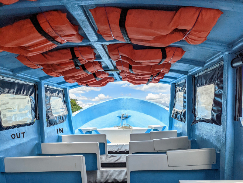 Interior of public boat on Lake Atitán. Boat has dark blue flaps on the windows. One flap is inside the boat and has an In label below it. Another window has the flap outside the boat and has a label out below it. 