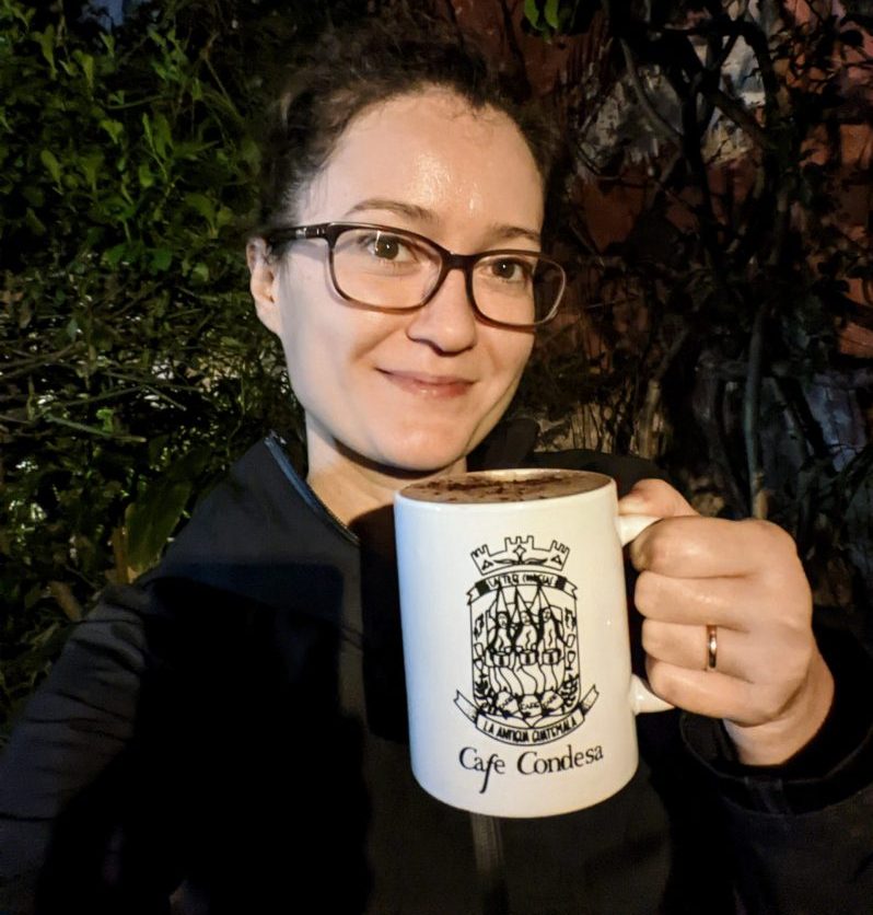 A women wearing dark glasses, holding a cup of hot chocolate with the Cafe Condesa logo.