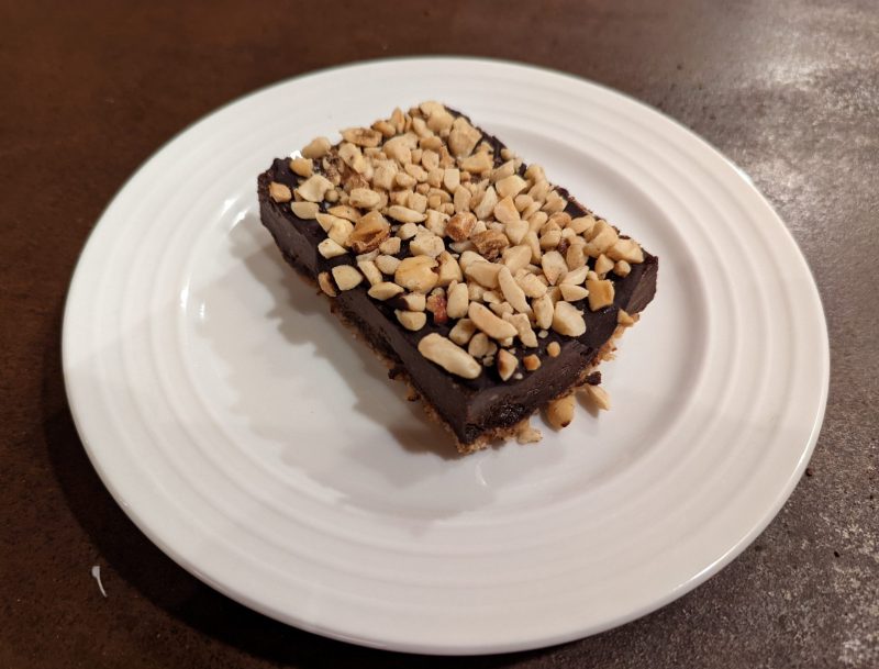 Rectangular dessert on a white plate, topped with peanuts. 