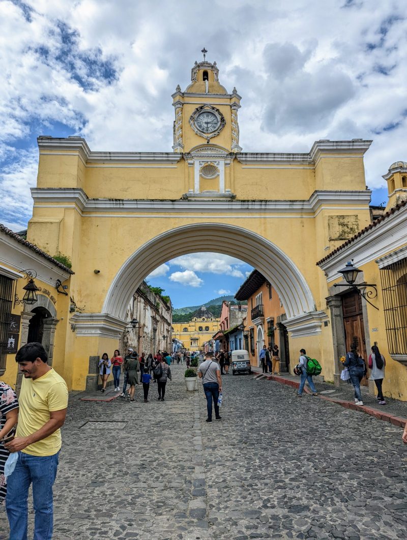 Picture of the yellow Santa Catalina Arch People are seen walking in the street below it. 