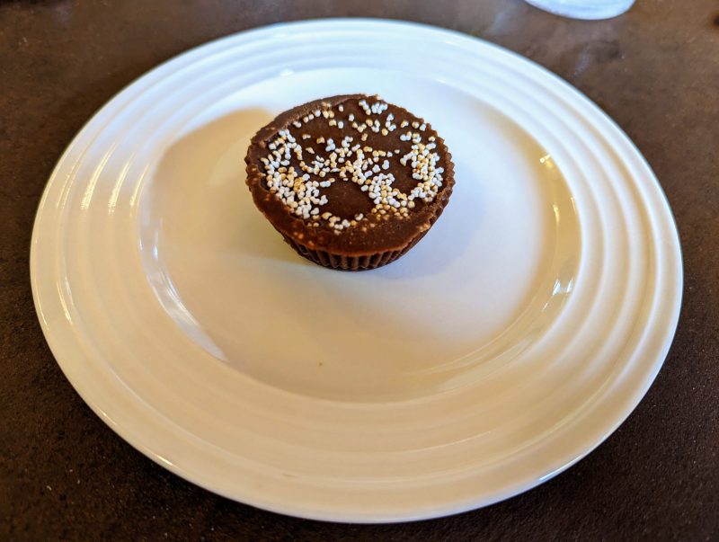 Round chocolate dessert with white and yellow sprinkles on a white plate. 