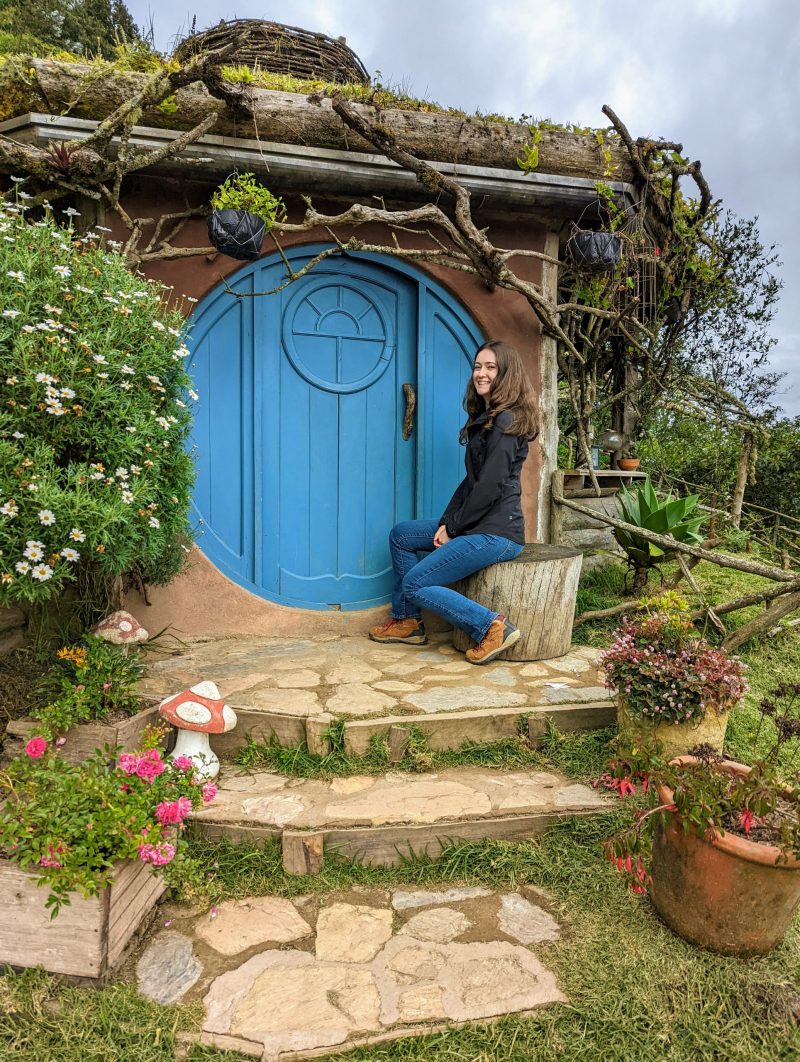 Jessica sitting in front of a hobbit style home. 