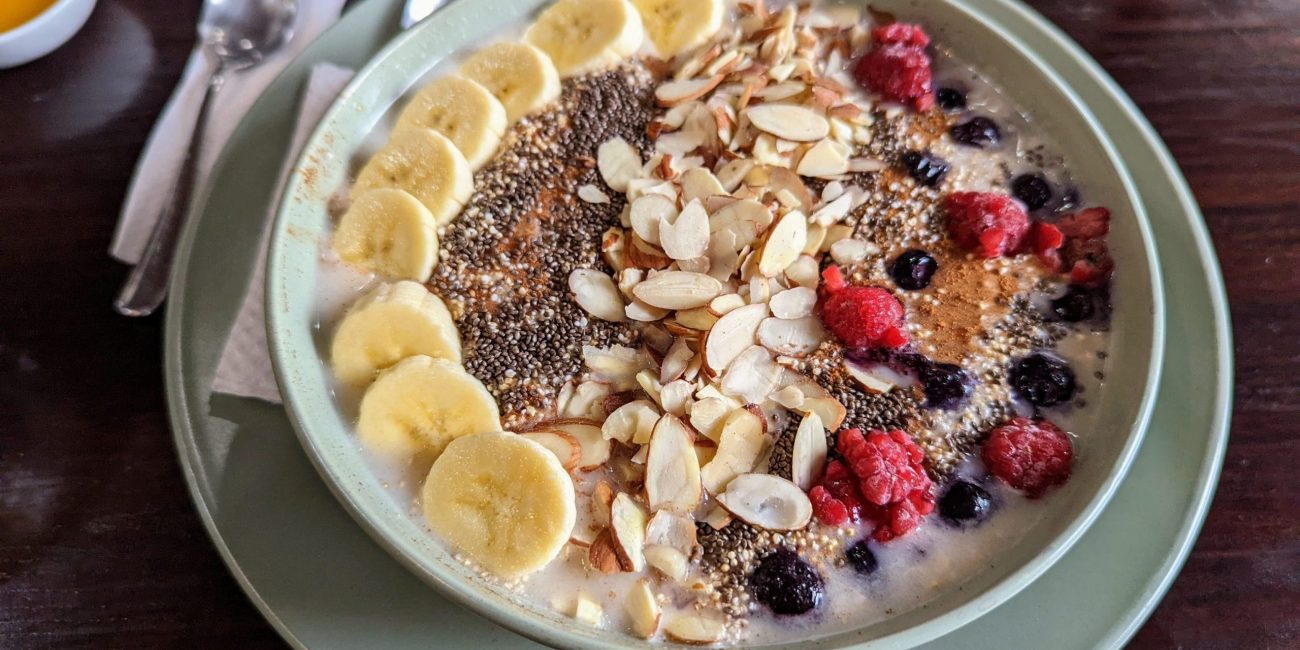 A bowl of oatmeal with bananas, berries chia seeds and almonds on top.