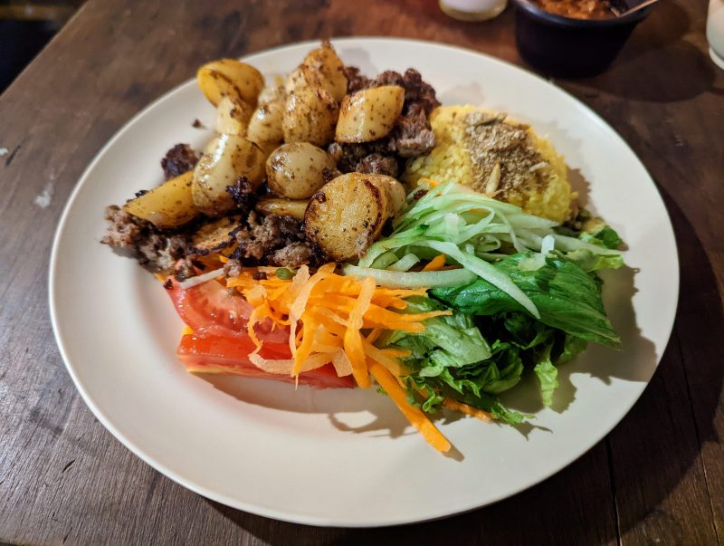 White plate with potatoes, greens, shaved carrots and yellow rice.