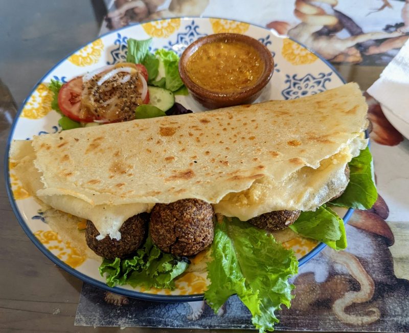 Quinoa balls are sticking out of wrap on a plate. A small bowl of orange curry sauce is on the plate. 